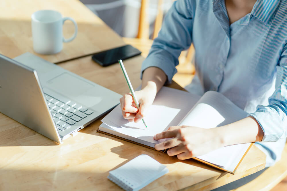 A woman is sitting at a table with a laptop and a pen