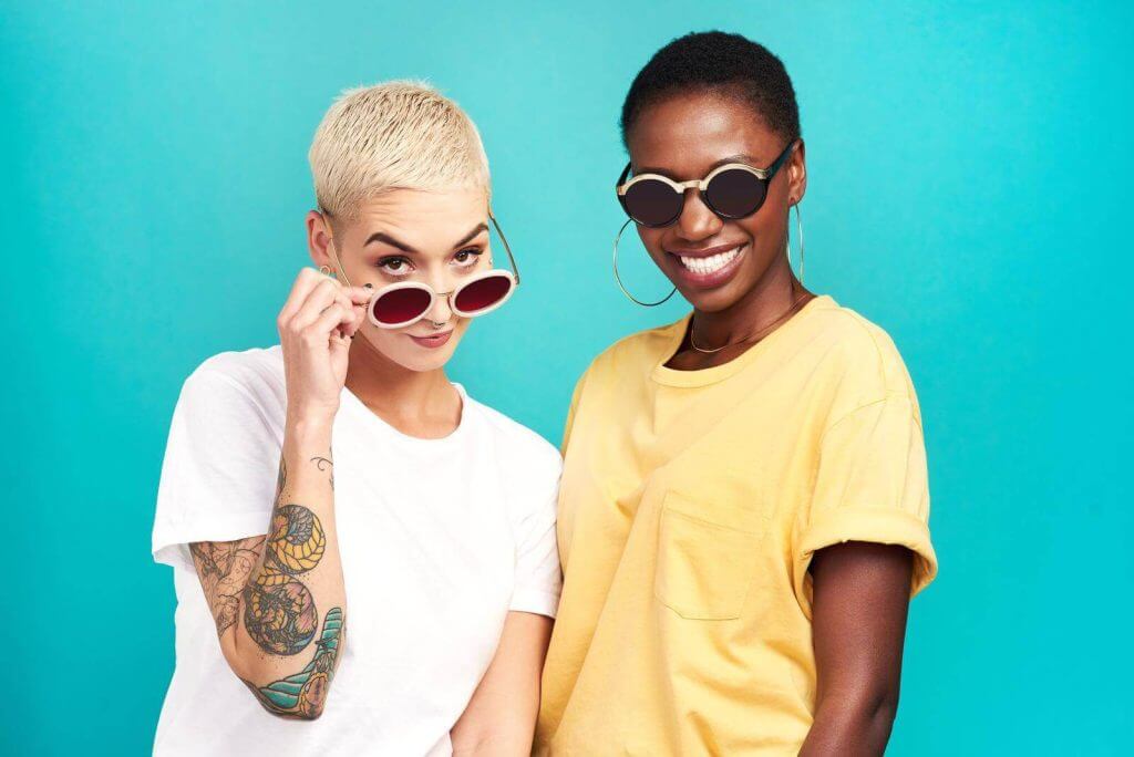 Two women with tattoos posing for a photo on a blue background