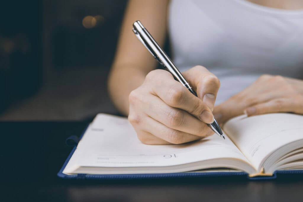 Person writing in a notebook with a pen