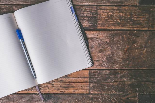 An open blank notebook with a blue pen on a wooden surface