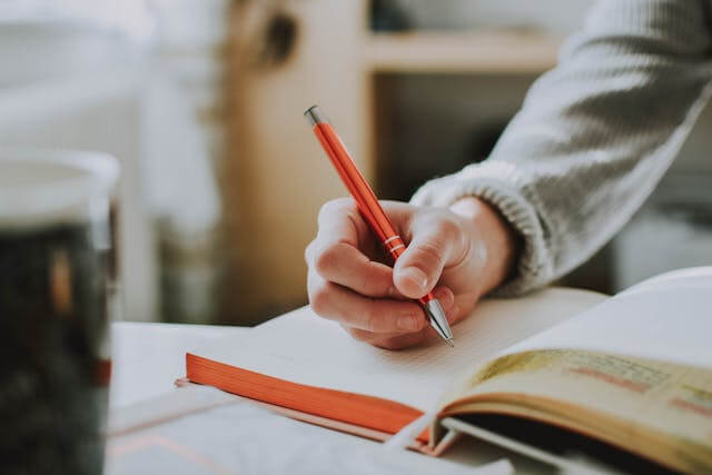 Person writing in a notebook with a red pen