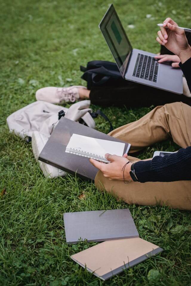 Person working on a laptop in a grassy area with notebooks around