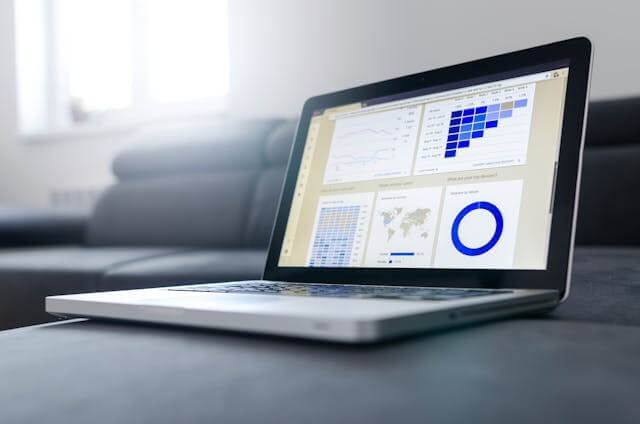 Open laptop displaying various data analytics charts and graphs including a heat map line graph world map and pie chart The laptop is placed on a dark colored surface