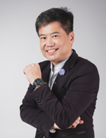 a person with short dark hair wearing a dark blazer and light shirt is smiling and posing with their right arm crossed over their chest against a plain light background.