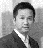 black and white headshot of an asian man in a suit, with a cityscape in the soft-focus background.