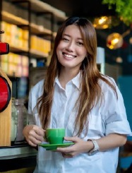 A woman smiling in front of a coffee shop.